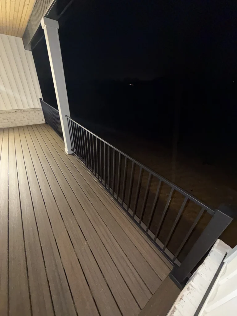 Completed Trex composite deck with black aluminum railing on a covered porch in Gray, TN at night
